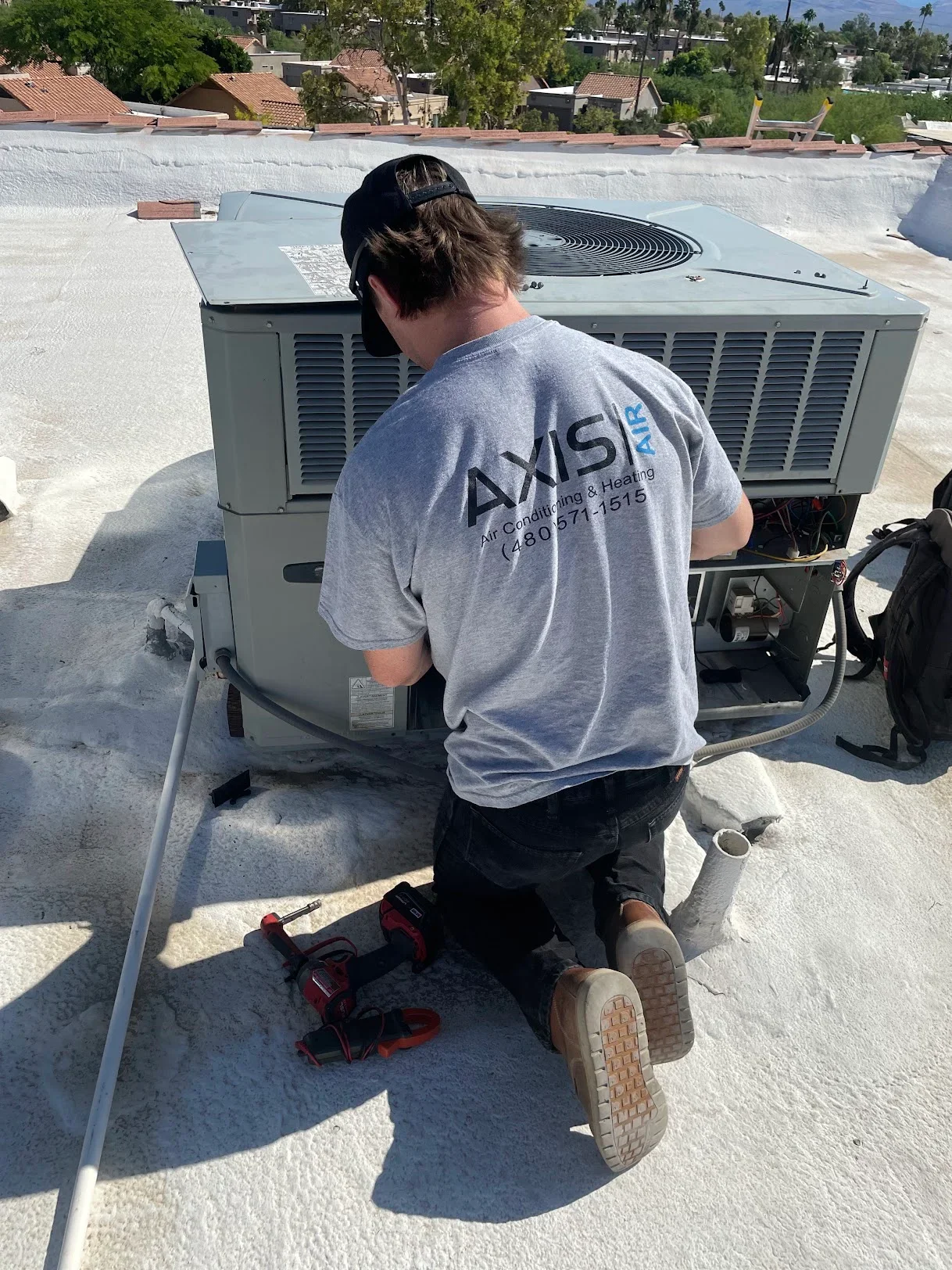 Technician installing rooftop AC condensing unit with refrigerant lines on flat roof