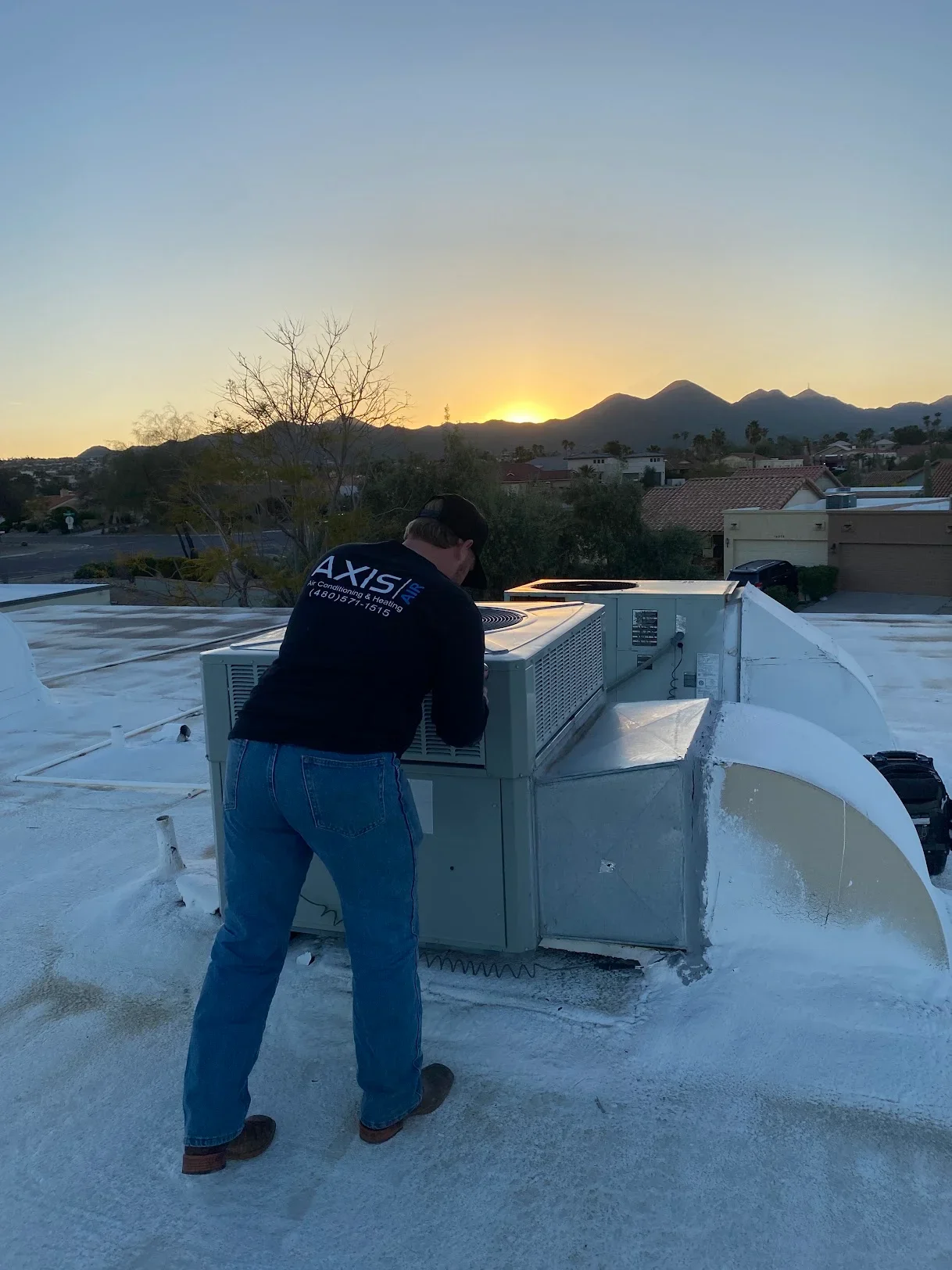 Technician installing rooftop HVAC unit on flat membrane roof with mountain backdrop